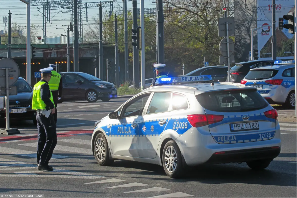 Policjant stoi przed radiowozem na skrzyżowaniu