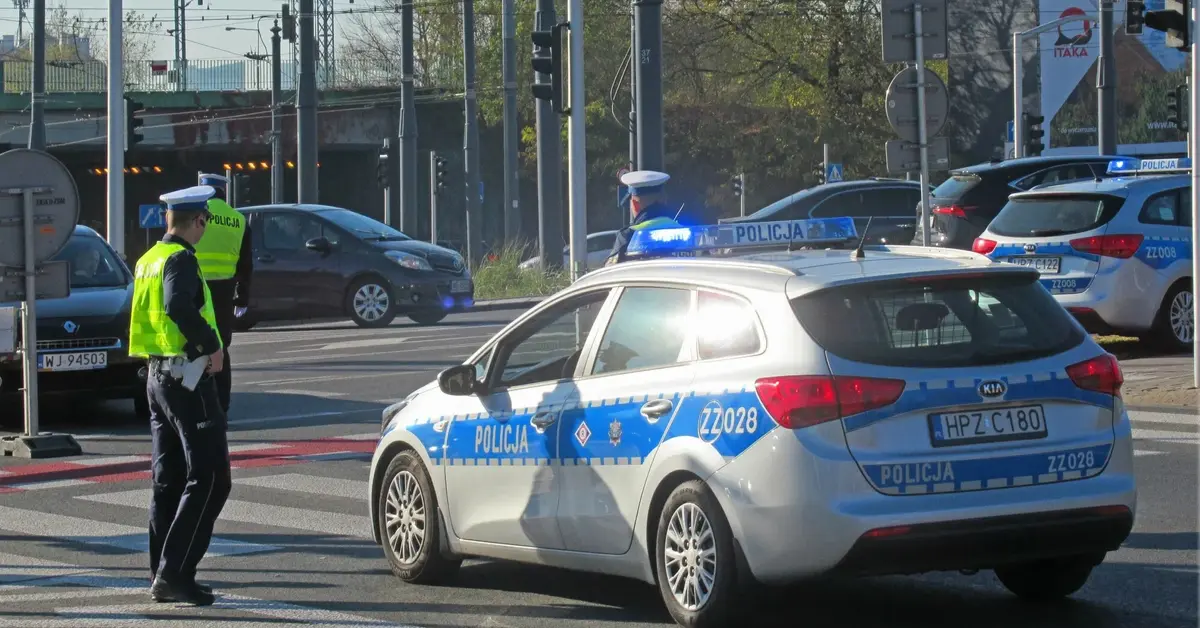 Policjant stoi przed radiowozem na skrzyżowaniu