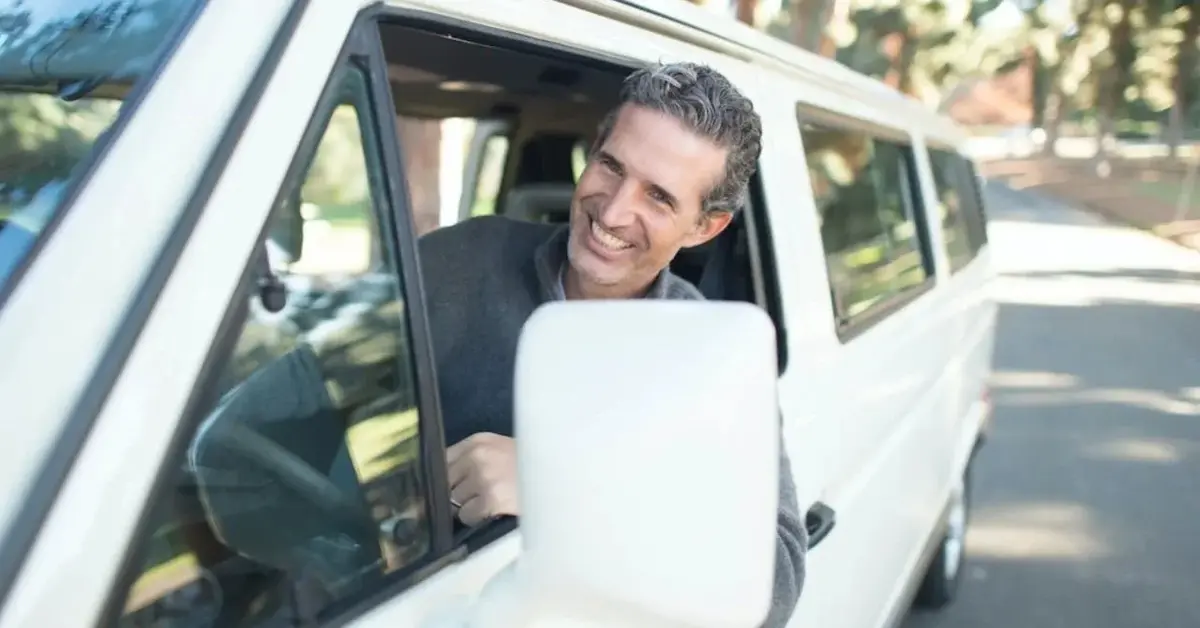 Uśmiechnięty mężczyzna za kierownicą białego samochodu z aktualną polisą OC