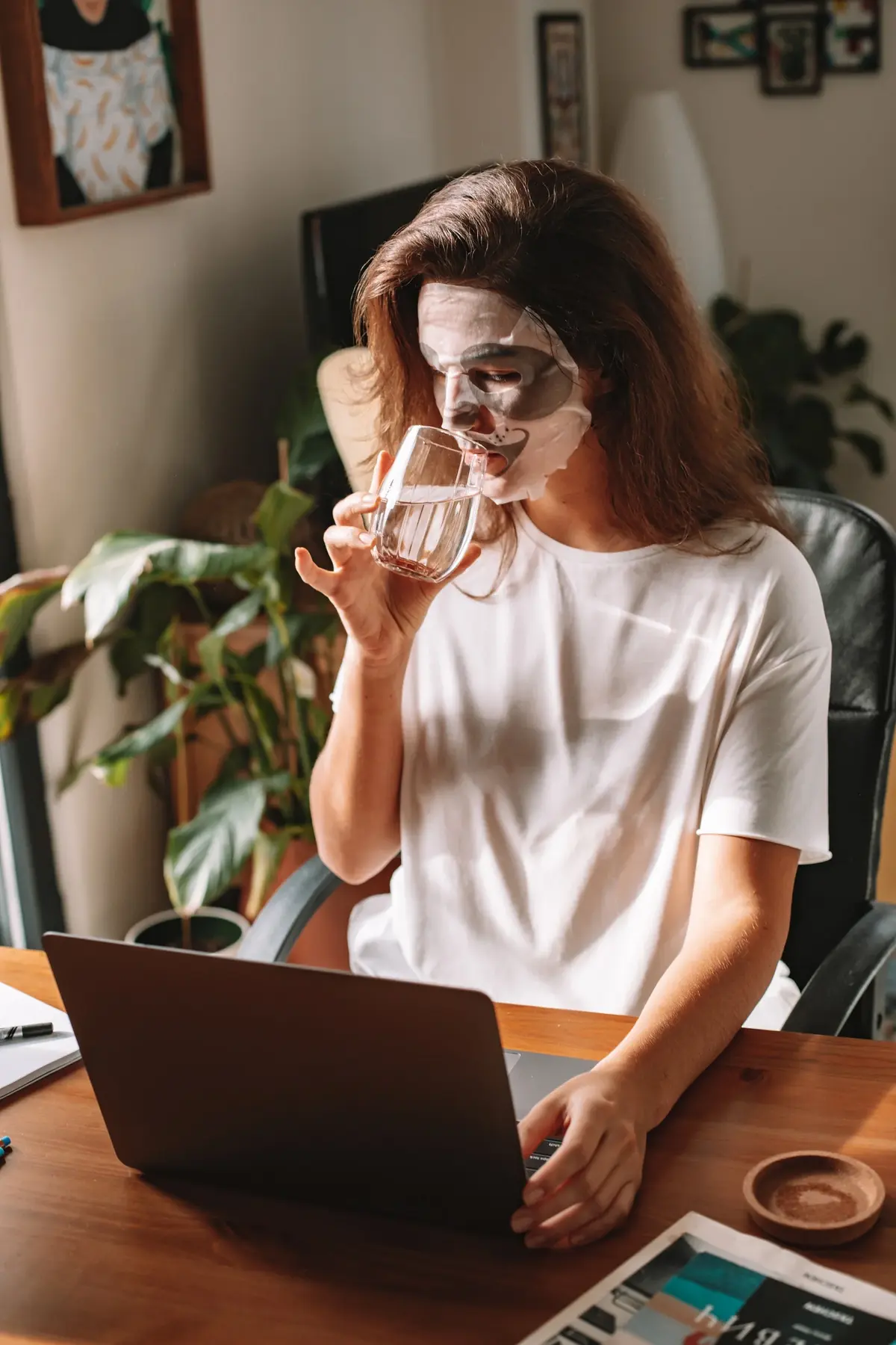 Kobieta z maseczką na twarzy, popia wodę i pracuje przy laptopie