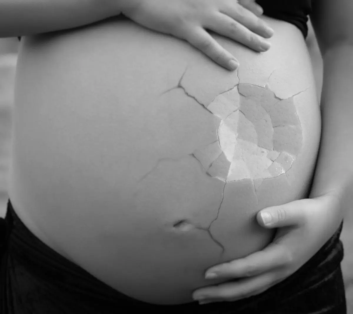 Kobieta w ciąży trzymająca się za brzuch na który naniesiona jest grafika przypominająca zbita skorupkę jajka