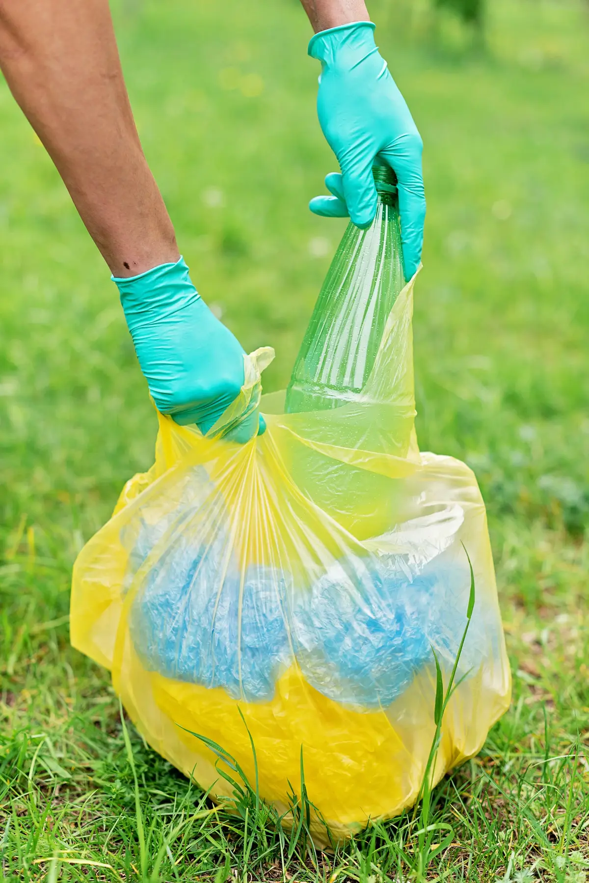Ktoś zbiera plastikowe śmieci w zielonych rękawiczkach do żółtego worka