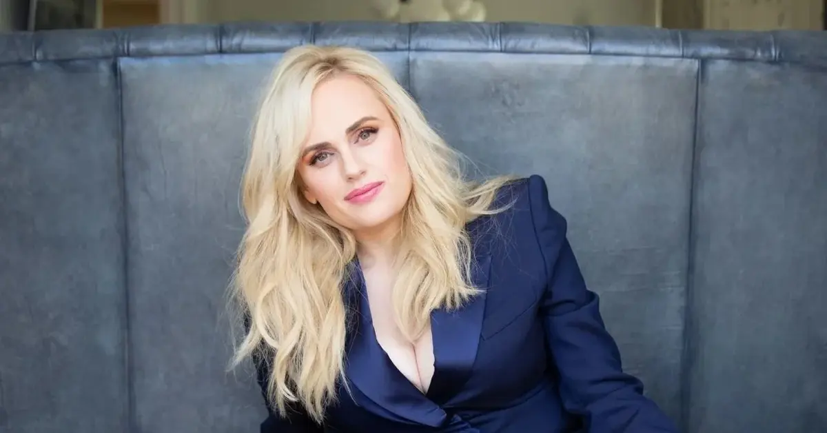 Rebel Wilson, prowadząca BAFTA 2022, w granatowej marynarce siedzi na szarym tle