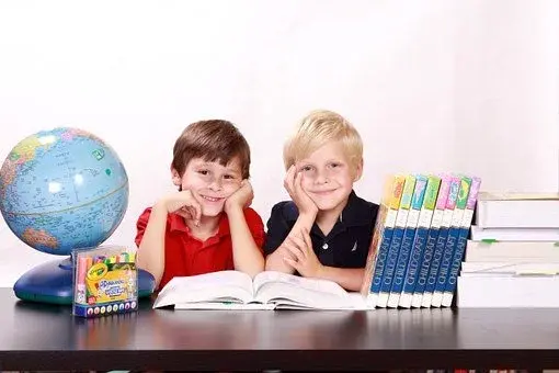 Uśmiechnięte dzieci opierające się o stół, na którym jest globus i zeszyty