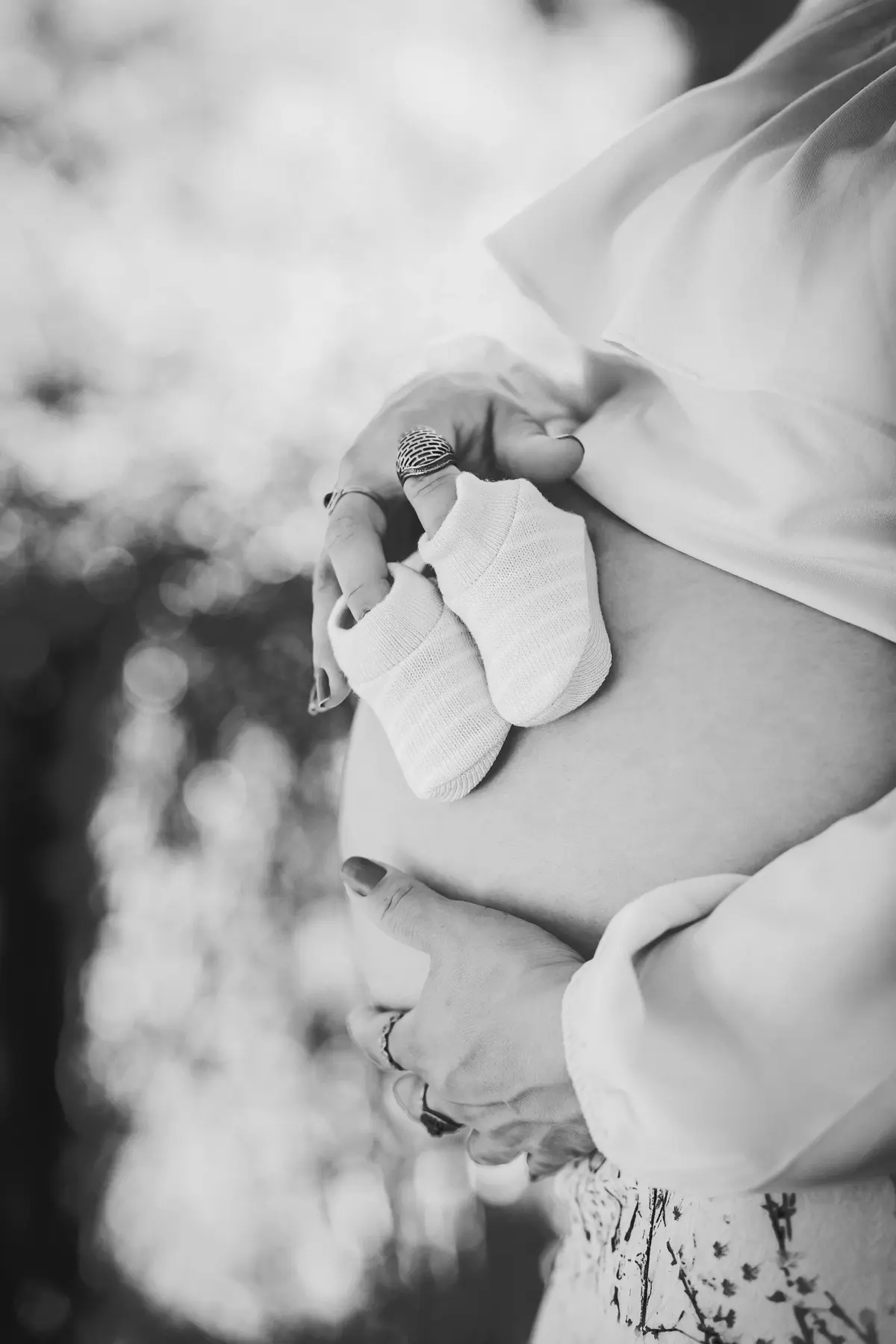 Kobieta trzyma ciążowy brzuch, w dłoni trzyma dziecięce skarpetki