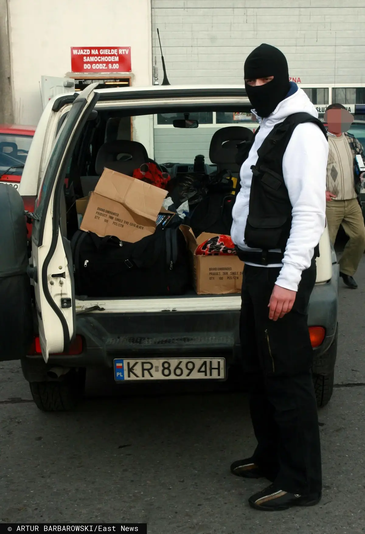 Mężczyzna w kominiarce stoi przy białym samochodzie