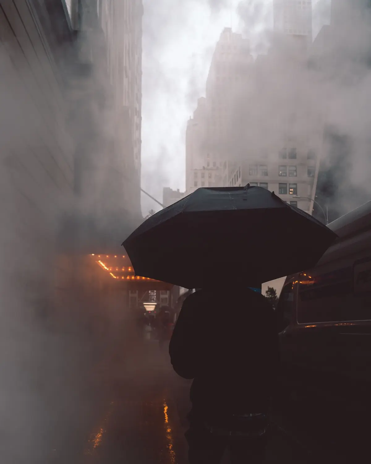 Smog w centrum miasta, osoba ubrana na czarno z czarnym parasolem idzie przez smog