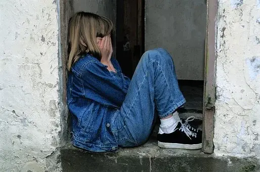 Smutna dziewczynka w jeansowym ubraniu, siedząca na ziemi
