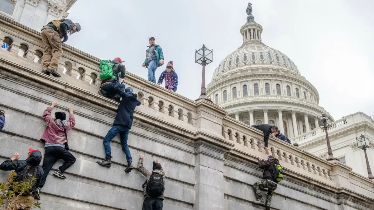Grupa ludzi wspinająca się na mur podczas Szturmu na Kapitol z 6 stycznia 2021 roku