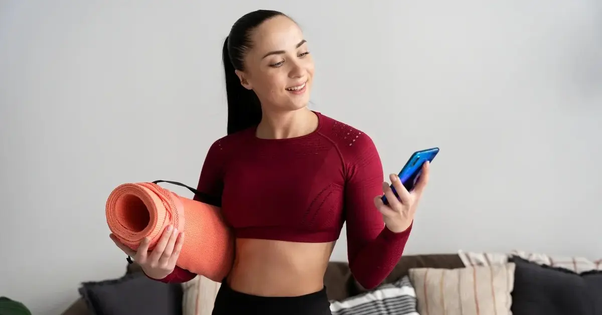 Młoda kobieta z matą do ćwiczeń pod pachą sprawdza w telefonie usługi online w efektywnym odchudzaniu