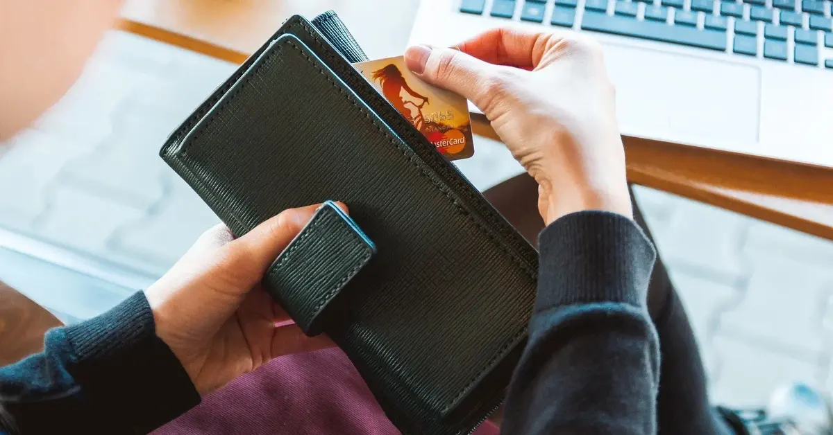 kobieta trzymająca czarny portfel z którego wyciąga kartę kredytową