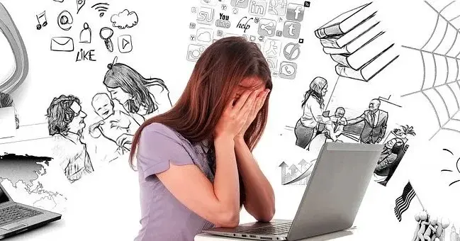 Kobieta przy laptopie z głową schowaną w dłoniach, za nią grafiki