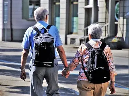 Para seniorów z plecakami w mieście, trzymająca się za ręce