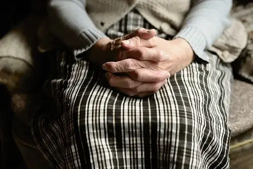 Starsza kobieta trzymająca dłonie splecione ze sobą na kolanach