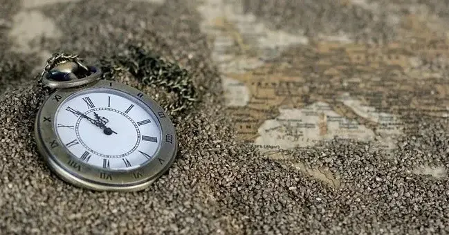 Zegar ze wskazówkami pokazującymi na kilka minut przed północą, leżący na piasku